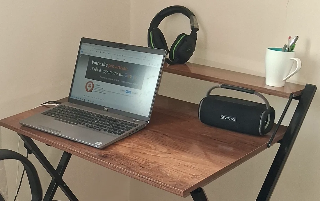 Le poste de travail où Sitigo est développé : un plateau d'appoint dans un coin de pièce, un ordinateur portable Dell affichant la page d'accueil de Sitigo, un casque, une enceinte portable et un mug de stylos.